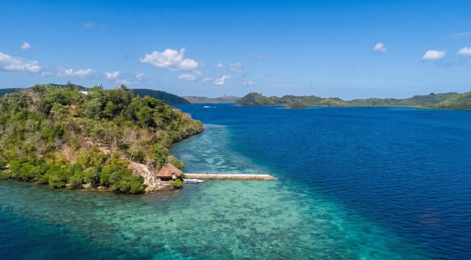 Wide aerial view of the island's dock reaching into the lagoon, mountains in the distance